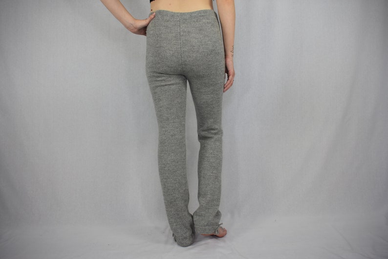 Puede incluir: Un pantal&oacute;n de punto gris jaspeado con dise&ntilde;o de cintura alta y una costura vertical visible en la parte central trasera. El pantal&oacute;n tiene una silueta ajustada que llega hasta los tobillos, confeccionado en un tejido con textura.
