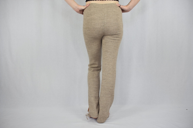 Puede incluir: Un pantal&oacute;n de tiro alto y largo completo en tejido de punto jaspeado de color marr&oacute;n claro s&oacute;lido. El pantal&oacute;n presenta una silueta ajustada en caderas y muslos con corte de pierna recta, cintura limpia y una costura central vertical visible.
