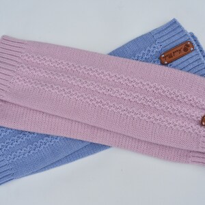 May include: A pair of knitted leg warmers in light pink and periwinkle blue. Each piece features a ribbed cuff at both ends and a central textured cable knit pattern. A small brown rectangular leather tag labeled Hand Made is attached.