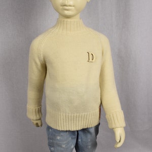 May include: A cream colored knitted sweater with a mock neck and a wooden letter 'D' on the front.