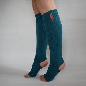 May include: A pair of teal, knee-high, ribbed knit leg warmers featuring an open heel and toe design. The leg warmers have a textured, knitted appearance and include a small, rectangular brown leather-like brand tag attached to the upper cuff.