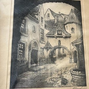 Puede incluir: Un grabado en blanco y negro que representa un patio europeo con edificios de piedra, un arco central y un pozo de piedra en primer plano. La escena presenta elementos arquitectónicos detallados, incluyendo ventanas, techos y un camino empedrado.