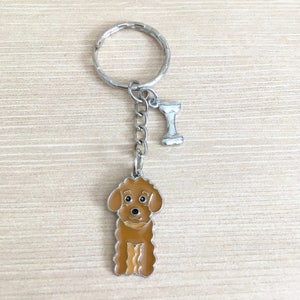 May include: A brown poodle keyring with a silver bone charm attached to a silver chain and ring.