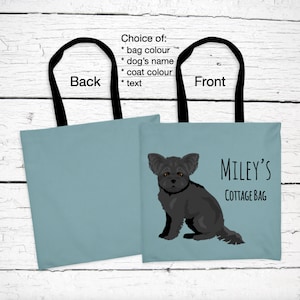Peut inclure: Un sac fourre-tout bleu avec des anses noires. Le devant du sac présente une illustration d'un Yorkshire Terrier noir et le texte "MILEY'S COTTAGE BAG".
