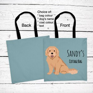May include: A light blue tote bag with black handles. The front of the bag features a cartoon illustration of a golden dog and the text "SANDY'S COTTAGE BAG". The back of the bag is solid light blue.