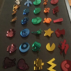 May include: A collection of colorful, reflective acrylic charms in various shapes, including stars, puzzle pieces, and abstract designs. The charms are in shades of blue, green, red, orange, and gold, with a mirrored finish.