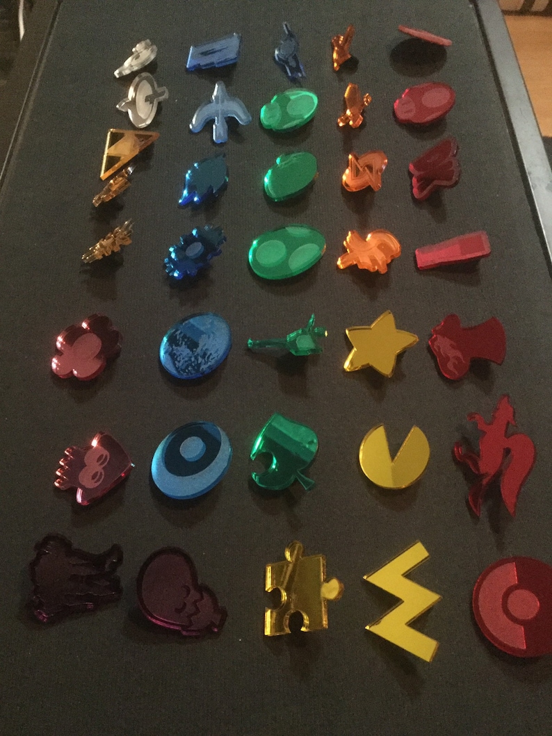 May include: A collection of colorful, reflective acrylic charms in various shapes, including stars, puzzle pieces, and abstract designs. The charms are in shades of blue, green, red, orange, and gold, with a mirrored finish.