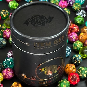 Puede incluir: Un recipiente cil&iacute;ndrico negro con una etiqueta dorada que dice "ITEM GET Illuminate Your Imagination" y una imagen dorada de un dado de 20 caras. El recipiente est&aacute; rodeado de dados de 20 caras de colores.