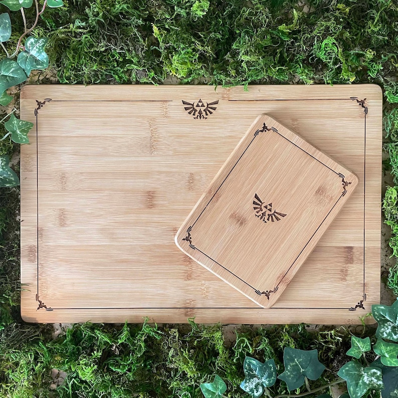 Puede incluir: Una tabla de cortar de bamb&uacute; con una tabla de cortar m&aacute;s peque&ntilde;a insertada. Ambas tablas tienen un borde decorativo y un dise&ntilde;o estilizado en el centro.