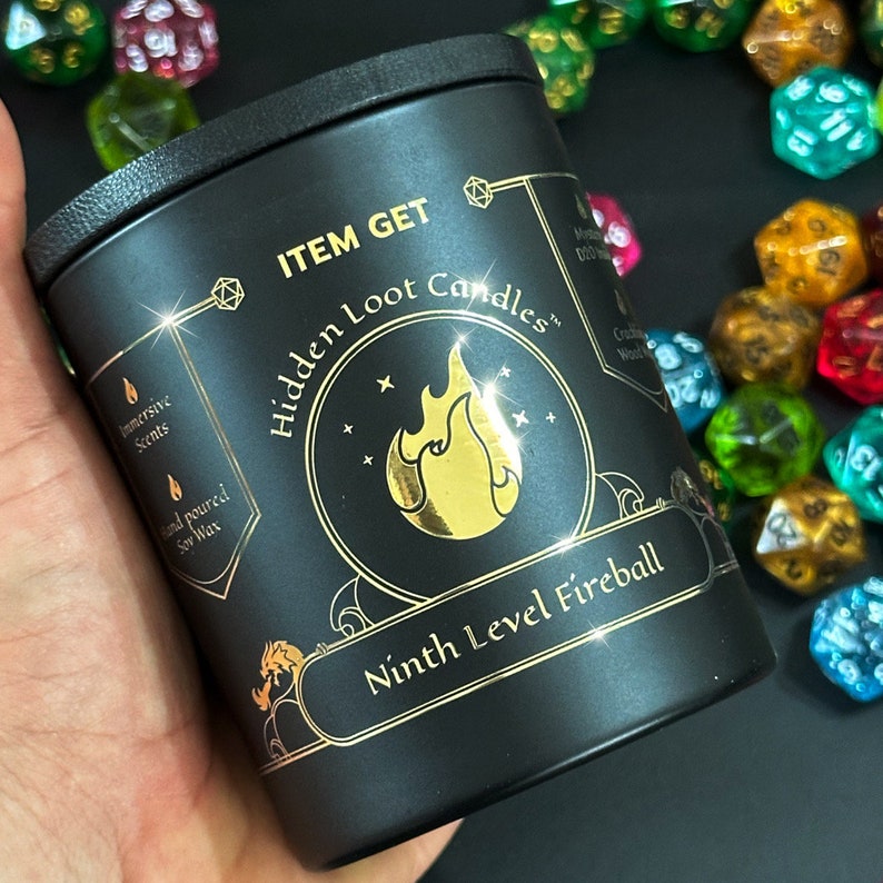Puede incluir: Tarro de vela negro con letras doradas que dicen "ITEM GET Hidden Loot Candles" y "Ninth Level Fireball". El tarro de vela est&aacute; rodeado de dados de colores.