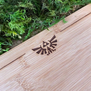 Puede incluir: Primer plano de una tabla de cortar de madera marr&oacute;n claro con un dise&ntilde;o triangular estilizado marr&oacute;n oscuro de un p&aacute;jaro con las alas extendidas. El dise&ntilde;o est&aacute; centrado en la tabla.