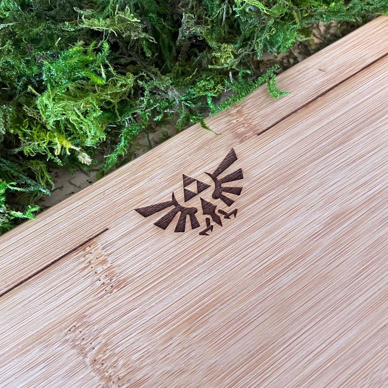 Puede incluir: Primer plano de una tabla de cortar de madera marr&oacute;n claro con un dise&ntilde;o triangular estilizado marr&oacute;n oscuro de un p&aacute;jaro con las alas extendidas. El dise&ntilde;o est&aacute; centrado en la tabla.
