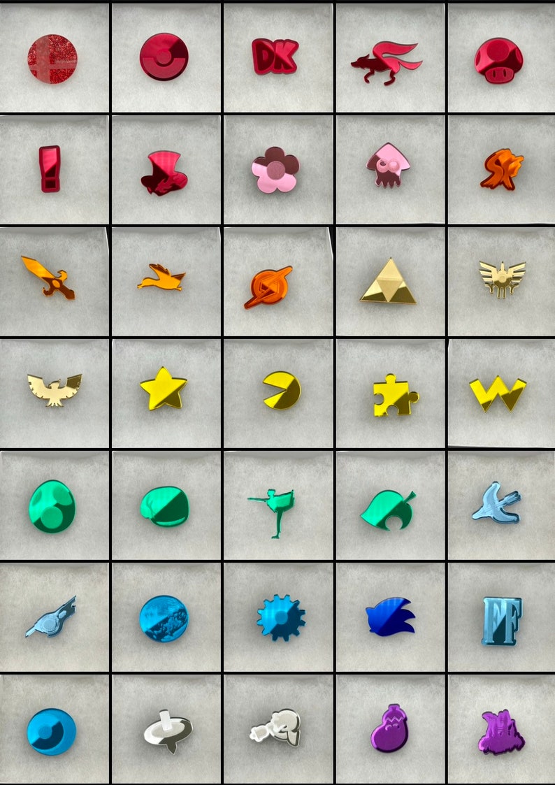 May include: A collection of colorful acrylic charms featuring various video game and pop culture icons. The charms include a mushroom, a star, a Pac-Man, and a puzzle piece, among others. Each charm is displayed in a square.