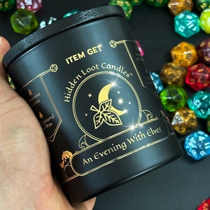 Puede incluir: Tarro de vela negro con letras doradas que dicen "ITEM GET Hidden Loot Candles" y "An Evening With Elves".