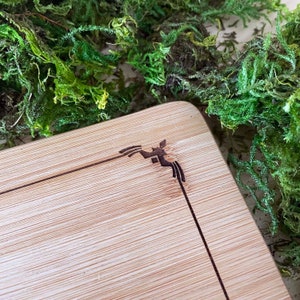 Puede incluir: Una tabla de cortar de bamb&uacute; natural con un dise&ntilde;o decorativo quemado en la esquina superior derecha. El dise&ntilde;o es un p&aacute;jaro estilizado con un patr&oacute;n geom&eacute;trico.