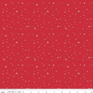 May include: Red fabric with a repeating pattern of white stars, dots, and floral shapes. The fabric is marked with inch measurements along the bottom edge. The text "Riley Blake Designs" is also visible.