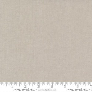 May include: A close-up of a plain, light beige fabric with a subtle texture. The fabric is smooth and has a slightly grainy appearance. The fabric is shown against a white background with a ruler marked in inches.