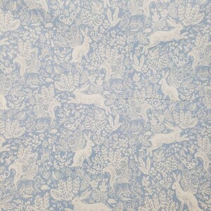 May include: Light blue fabric with a repeating pattern of white rabbits and foliage. The design features running and seated rabbits amidst detailed floral and plant elements, creating a whimsical, nature-inspired print. Ideal for home decor or crafting projects.