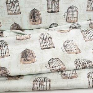 May include: Fabric with a repeating pattern of birdcages in shades of brown and gray on a light green background. The birdcages are detailed with bars and doors, and the background has a subtle, vintage newspaper print.