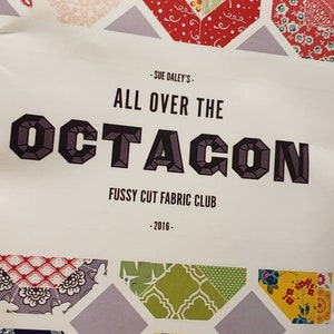 May include: A white flyer with the text "ALL OVER THE OCTAGON" in large, dark gray block letters. The flyer also includes the text "FUSSY CUT FABRIC CLUB" and "2016". The flyer is decorated with colorful octagonal fabric patterns.