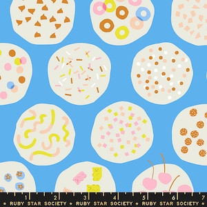 May include: A blue fabric with a repeating pattern of white circles with different colorful designs. The designs include sprinkles, chocolate chips, gummy bears, cherries, and donuts.