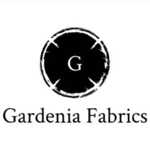 May include: A black and white logo for Gardenia Fabrics. The logo features a circular design with a distressed outer edge, enclosing a black circle with the letter "G" in white. Below the logo is the text "Gardenia Fabrics" in a serif font.