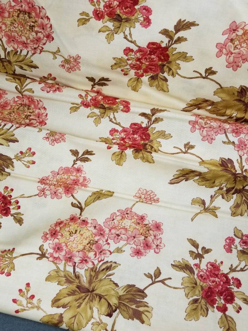 May include: A cream-colored fabric with a floral pattern. The flowers are pink and red with brown leaves.