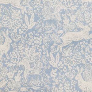May include: Light blue fabric with a repeating pattern of white rabbits, squirrels, flowers, and foliage. The design has a vintage, storybook aesthetic, with detailed illustrations of woodland creatures and plants.