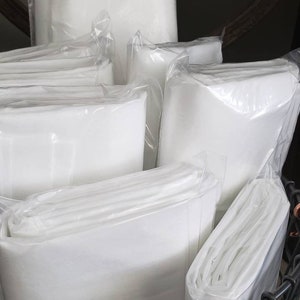 May include: A black wire basket filled with white fabric squares wrapped in clear plastic. The fabric squares are folded and stacked in the basket.