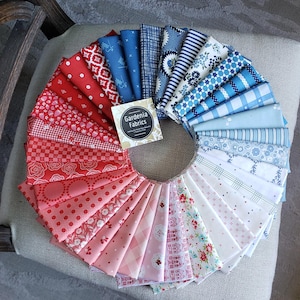May include: A circular arrangement of folded fabric squares in a gradient from red to pink to white and blue. The patterns include dots, stripes, florals, and geometric shapes. A square label in the center reads Gardenia Fabrics.