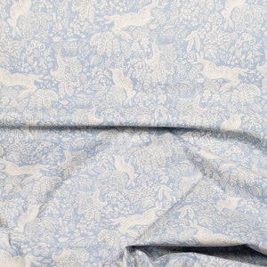 May include: Light blue fabric with a repeating pattern of white hares, birds, and foliage. The design is detailed and creates a whimsical, nature-inspired aesthetic. The fabric is folded, showing its texture and drape.