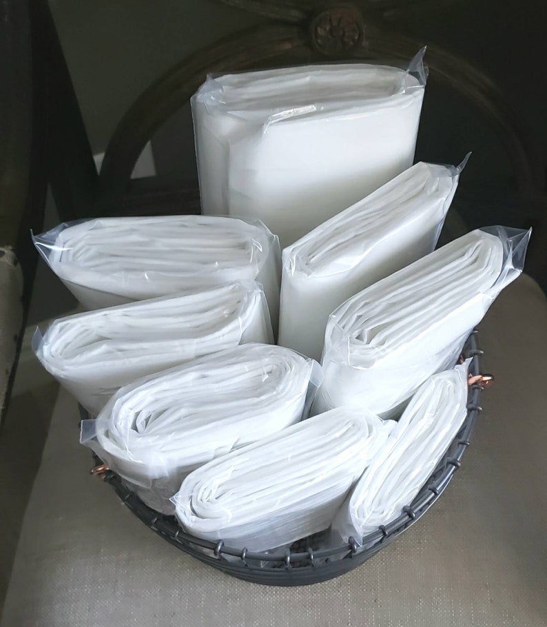 May include: A close-up of a wire basket filled with white fabric squares, folded and wrapped in clear plastic. The fabric squares are stacked neatly in the basket.