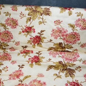 May include: A cream-colored fabric with a floral pattern. The flowers are pink and red with brown leaves.