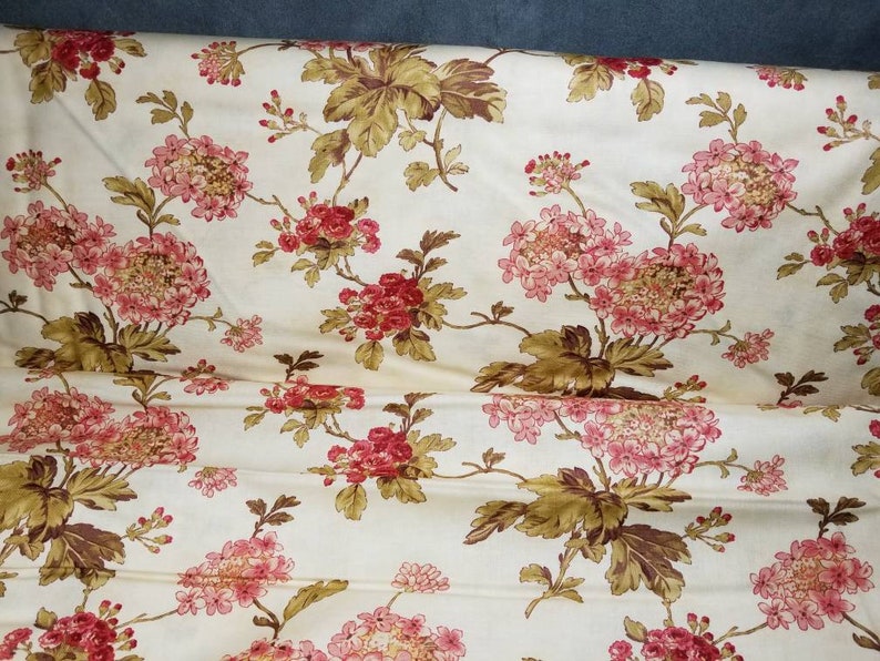 May include: A cream-colored fabric with a floral pattern. The flowers are pink and red with brown leaves.