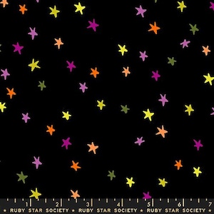 May include: A black fabric featuring a scattered pattern of hand-drawn stars in vibrant shades of yellow, orange, purple, and olive green. A ruler at the bottom shows measurements in inches, with the text Ruby Star Society printed repeatedly.
