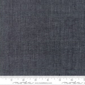 May include: A close-up of a dark gray fabric with a subtle texture. The fabric is measured with a ruler in inches, with the text "moda" printed on the ruler.