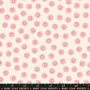 May include: A cream-colored fabric with a repeating pattern of pink smiley faces with orange smiles. The fabric is from Ruby Star Society.