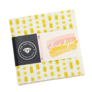 May include: A pack of 42 5-inch fabric squares with a yellow and white polka dot pattern. The pack is labeled "First Light Collaborative Collection" by Ruby Star Society.