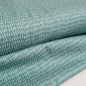 May include: A roll of fabric in a teal color with a pattern of small, vertical white dashes. The fabric is folded over, showing the texture and design. The background is a plain white surface.