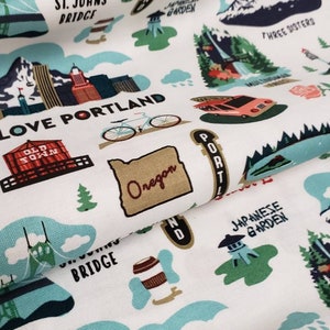 May include: A white fabric with a repeating pattern of illustrations depicting various landmarks and symbols of Portland, Oregon. The illustrations include a bicycle, a food truck, a bridge, a mountain range, a Japanese garden, and the words "Love Portland".