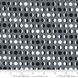 May include: Gray fabric with a repeating pattern of black, white, and gray moon phases. The fabric has a ruler along the bottom edge, with the Moda Fabrics logo and website address.