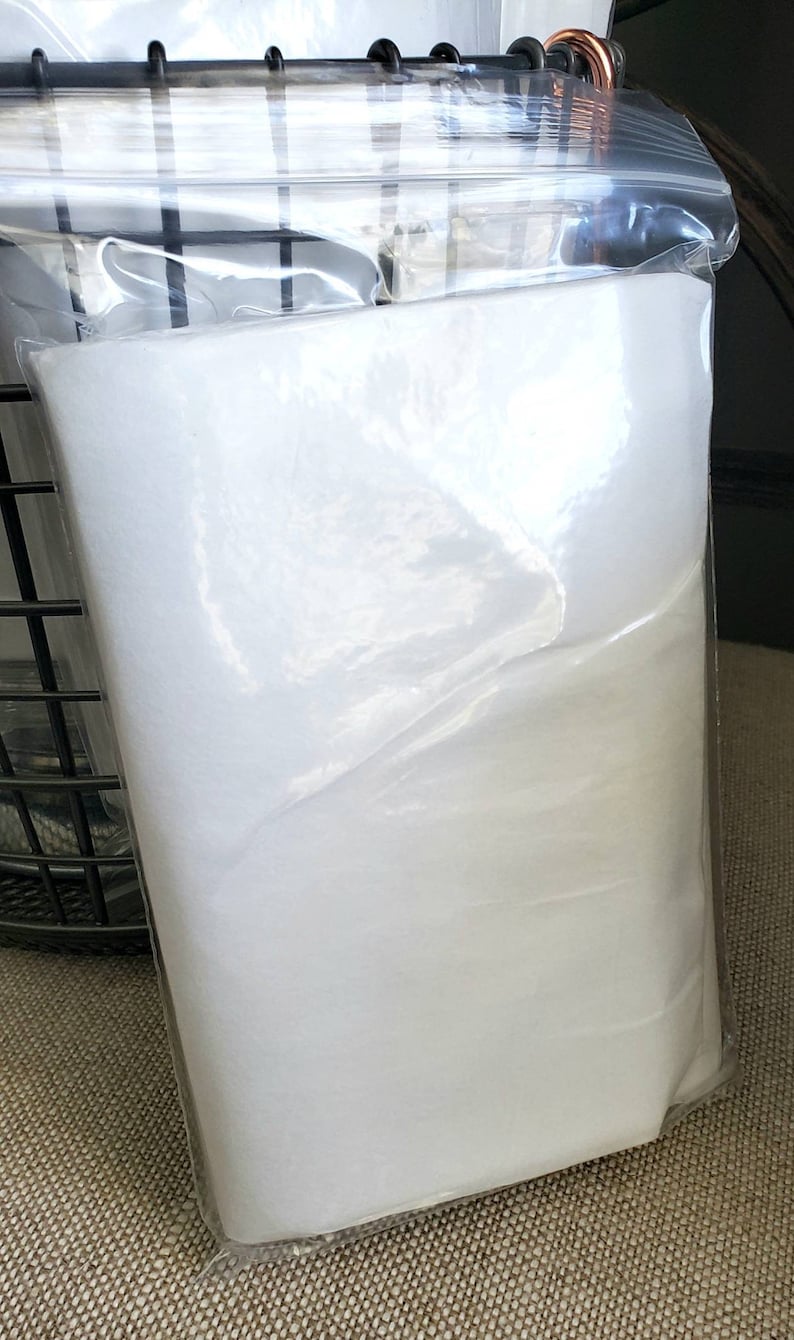 May include: A white fabric sheet is packaged in a clear plastic bag. The bag is sealed at the top and the fabric sheet is folded inside.