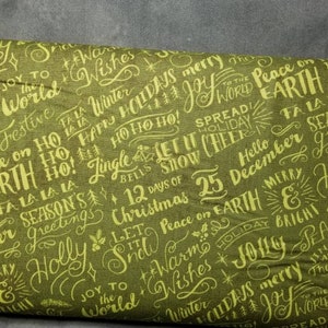 May include: Green fabric with a festive Christmas pattern featuring a variety of holiday greetings and phrases in a handwritten style. The text includes "Joy to the World", "Peace on Earth", "Happy Holidays", "Let it Snow", "Warm Wishes", and "Merry Christmas".