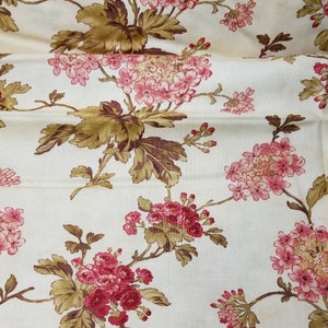 May include: A white fabric with a floral pattern. The flowers are pink and red with brown leaves. The fabric has a subtle texture.