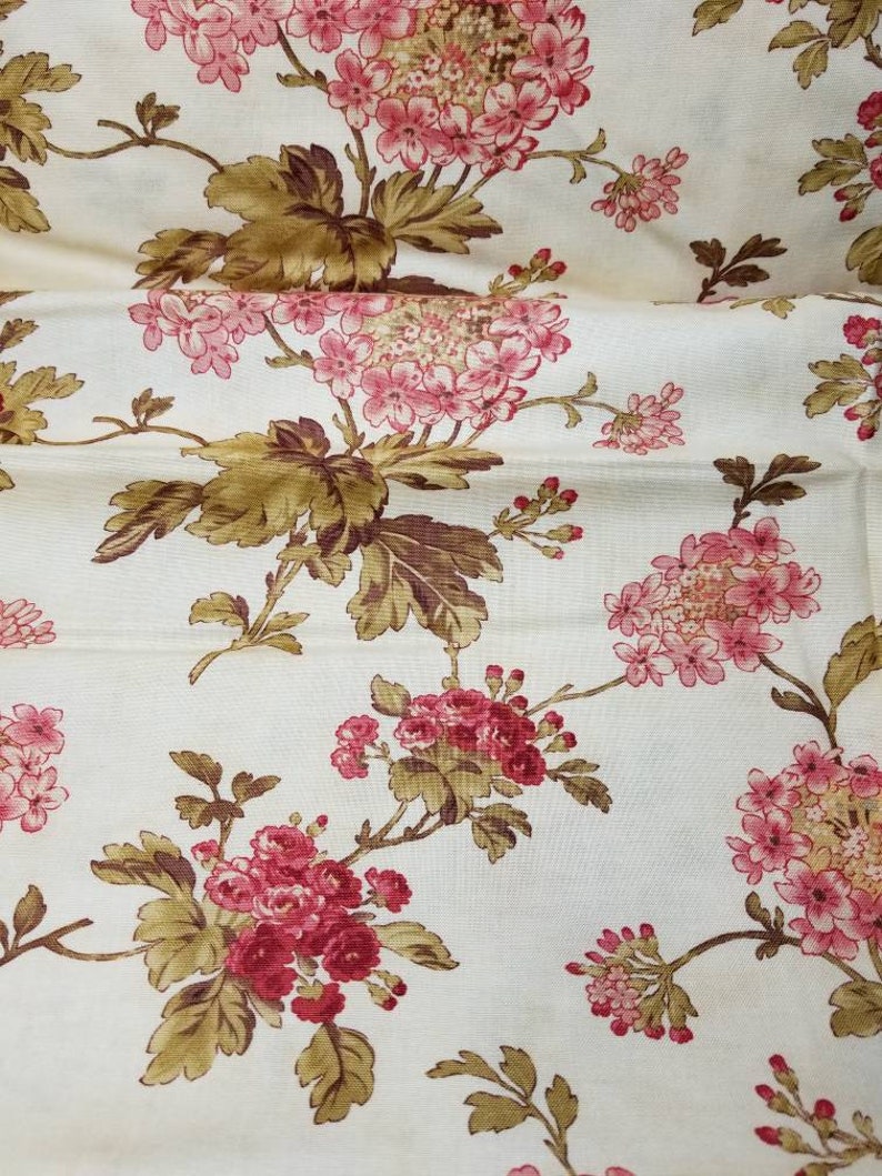 May include: A white fabric with a floral pattern. The flowers are pink and red with brown leaves. The fabric has a subtle texture.