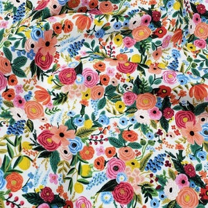 May include: A white fabric with a floral pattern featuring pink, red, orange, yellow, blue, and green flowers. The fabric is perfect for crafting, quilting, and sewing projects.