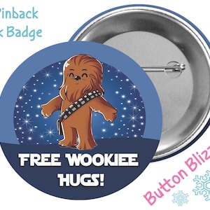 May include: A 3-inch pinback park badge featuring a cartoon Chewbacca with the text "Free Wookiee Hugs!" against a blue background with white stars.