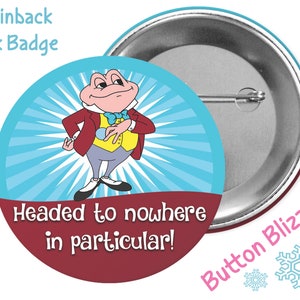 May include: A 3-inch pinback button featuring a cartoon frog wearing a red jacket, yellow vest, and blue bow tie. The frog is standing on a blue background with white rays emanating from behind him. The text "Headed to nowhere in particular!" is printed in white on a maroon background.