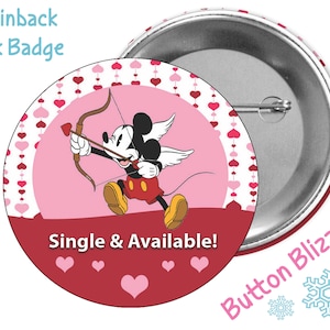 May include: A 3 inch pinback button featuring Mickey Mouse dressed as Cupid with angel wings, holding a bow and arrow. The background is pink with a pattern of white hearts. The text "Single & Available!" is printed in white on a red banner at the bottom of the button.
