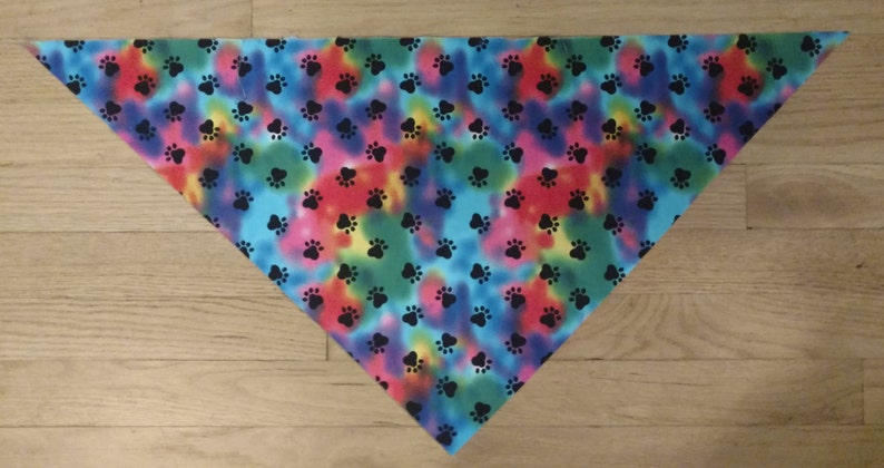 May include: A triangular bandana with a tie-dye pattern in shades of blue, green, red, and yellow. The bandana is covered in black paw prints.